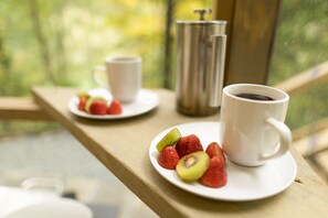 Desayuno con una taza de café y un plato de fresas y kiwi sobre una mesa de madera junto a una ventana.