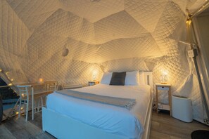A cozy, tent-like bedroom with a bed, bedside lamps, and a small table with a chair.