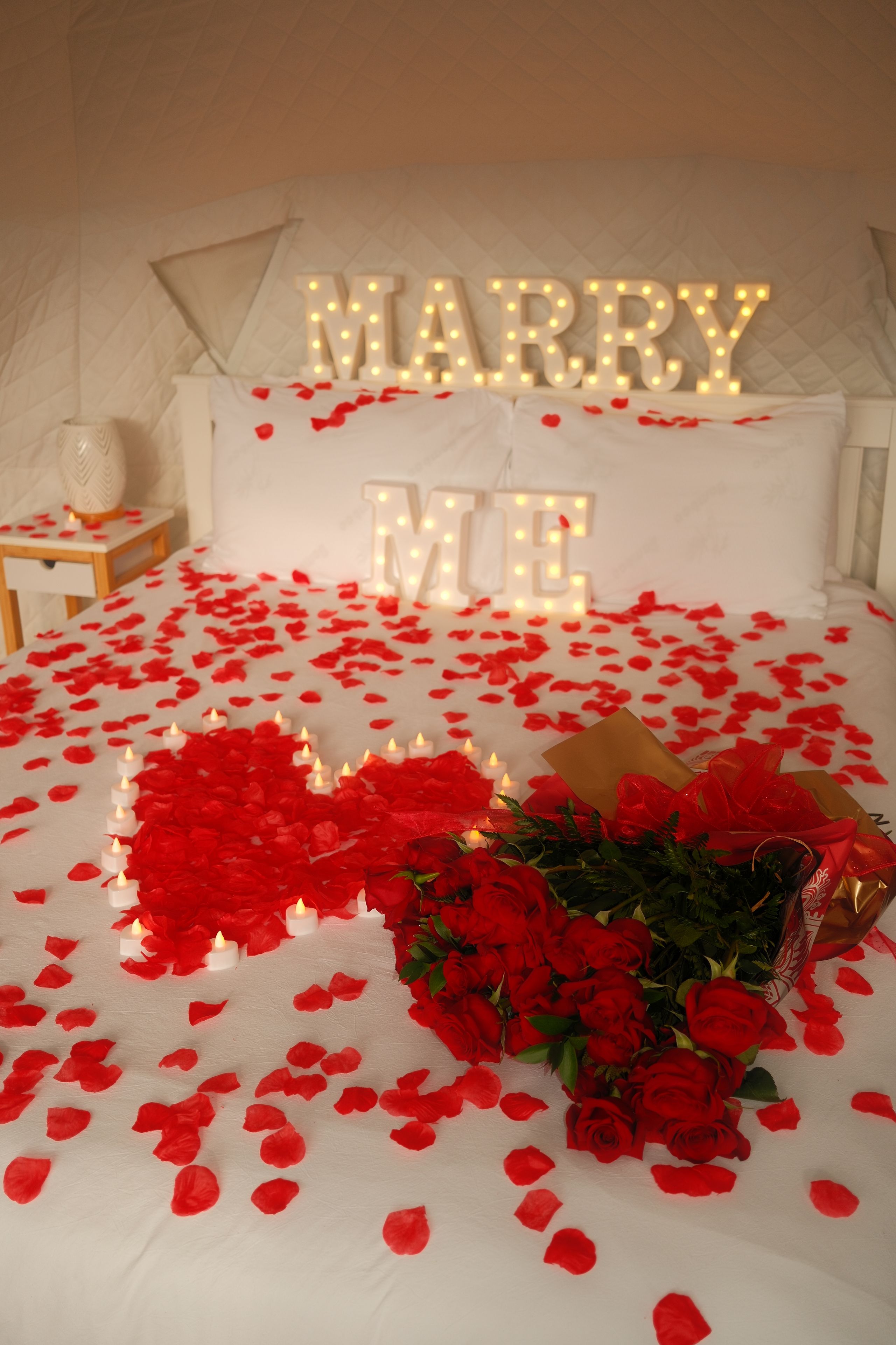 Un lit décoré de pétales de roses disposés en forme de cœur et agrémenté d’un bouquet de roses rouges.