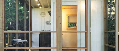 Una habitación con interior de madera, una pequeña mesa con sillas y una ventana con vistas a árboles.