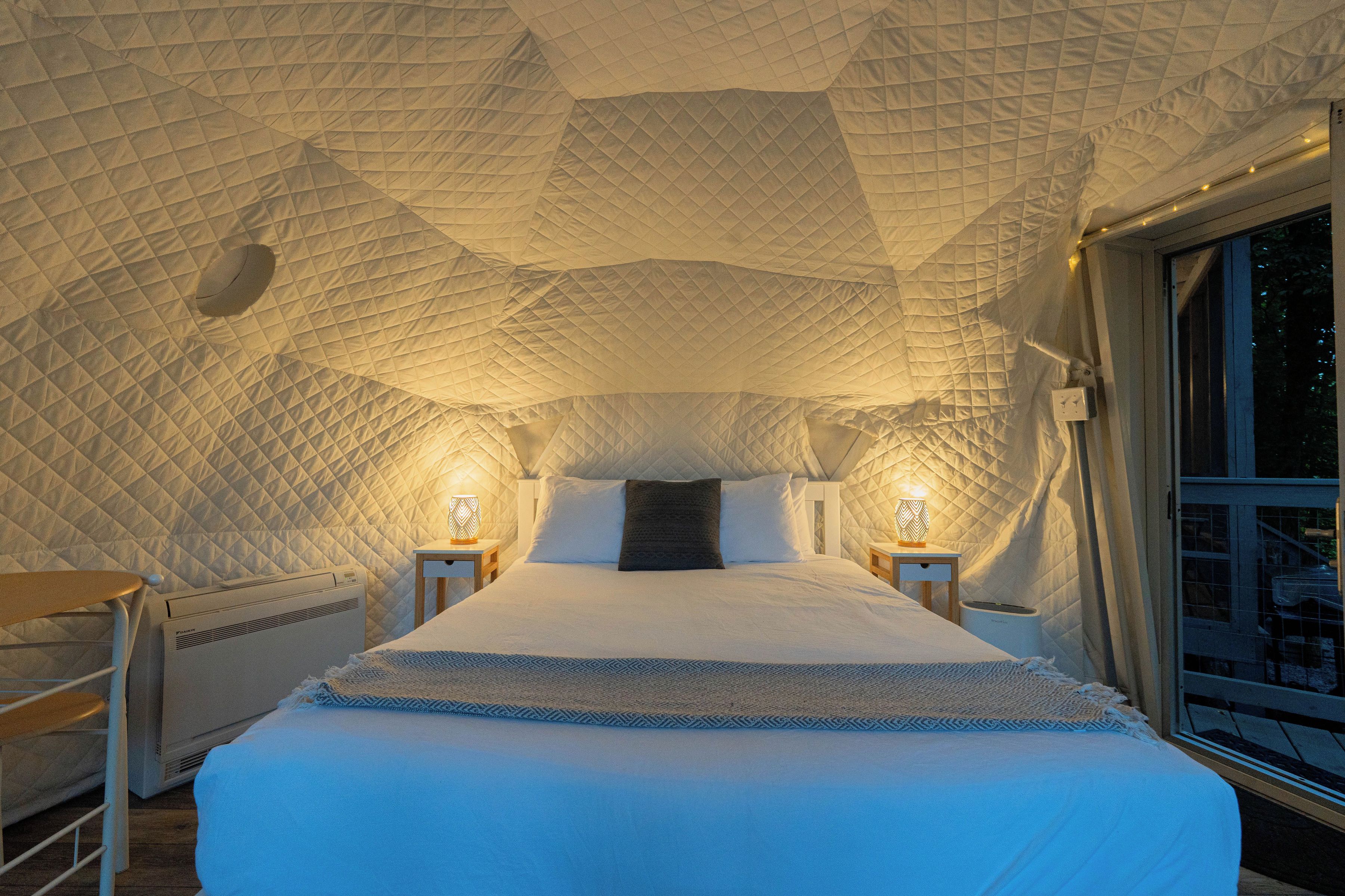 A room with a geometric patterned ceiling, a bed with white bedding, two bedside tables with lamps, and a window with a view.