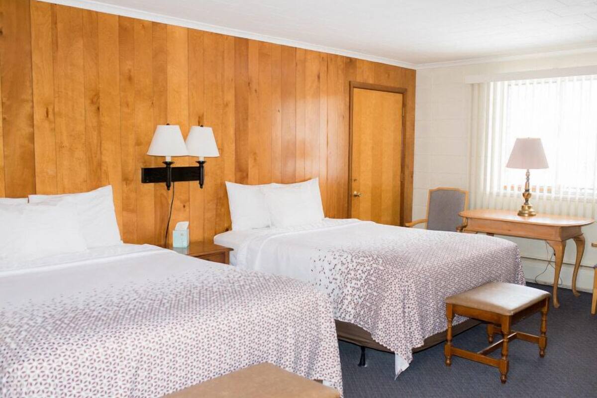 Habitación de hotel con dos camas, cabecero de madera, un escritorio con silla y ventana con persianas.