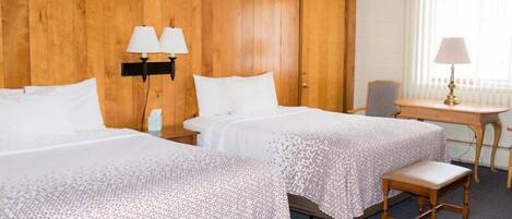 Habitación de hotel con dos camas, cabecero de madera, un escritorio con silla y ventana con persianas.