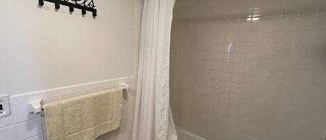 A bathroom with a white tiled wall, a towel rack with a towel, and a shower curtain.