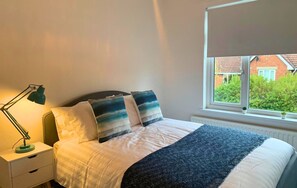 Une chambre à coucher avec un lit, une table de chevet, une lampe et une fenêtre donnant sur un paysage verdoyant et des bâtiments.