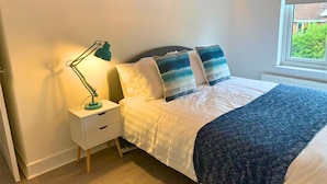 A bedroom with a bed, a nightstand, a lamp, and a window with a view of greenery. - Consett Shotley Bridge, Stylish & Modern Two Bedroom Apartment (Consett)