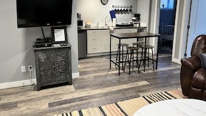 A modern kitchen with a flat-screen TV, a bar area with stools, and a dining table. - The Cedar Suite (Yellowhead County)