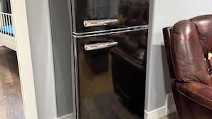 A black Galanz refrigerator in a room with a brown leather chair and a framed sign on the wall. - The Cedar Suite (Yellowhead County)