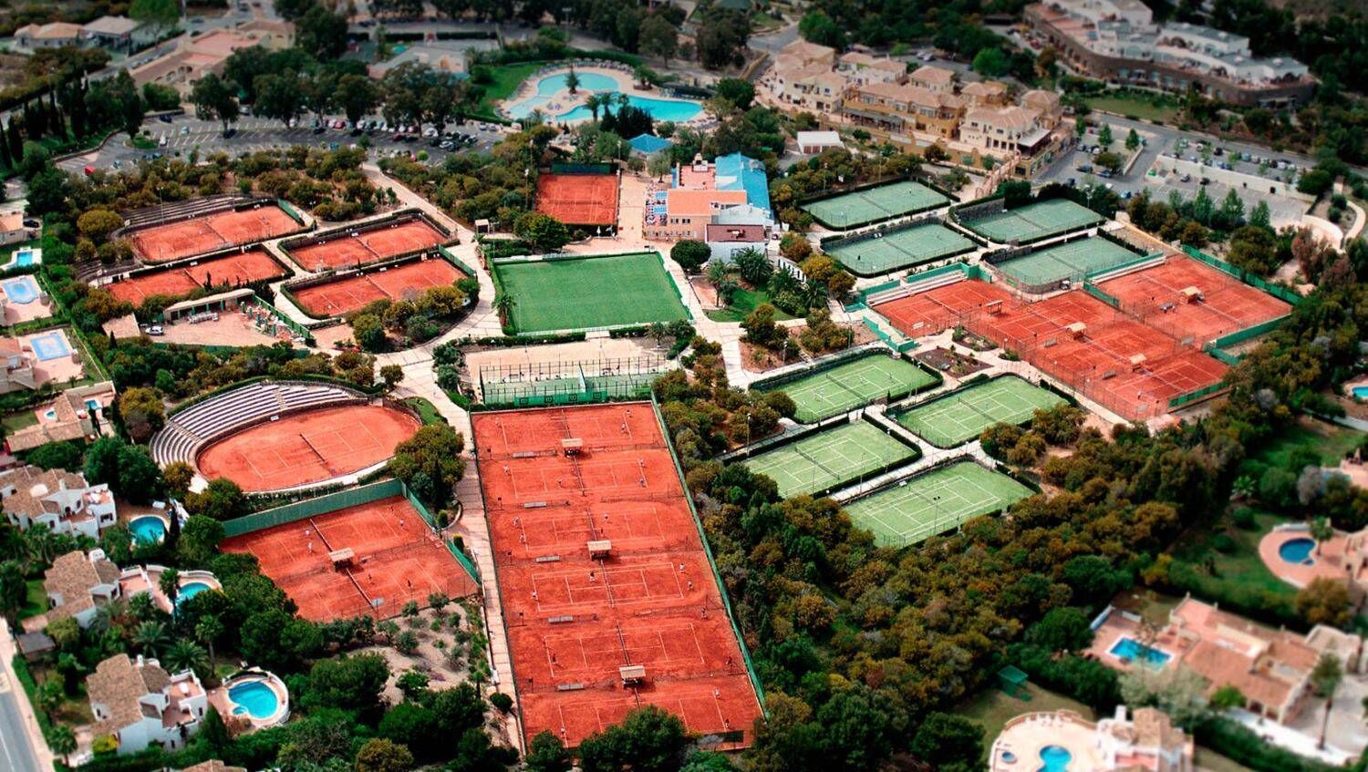 An aerial view of a sports complex with multiple tennis courts, a swimming pool, and surrounding residential buildings.