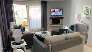 Ein modernes Wohnzimmer mit einer Couch, Sesseln, einem Couchtisch und einem an der Wand befestigten Fernseher.