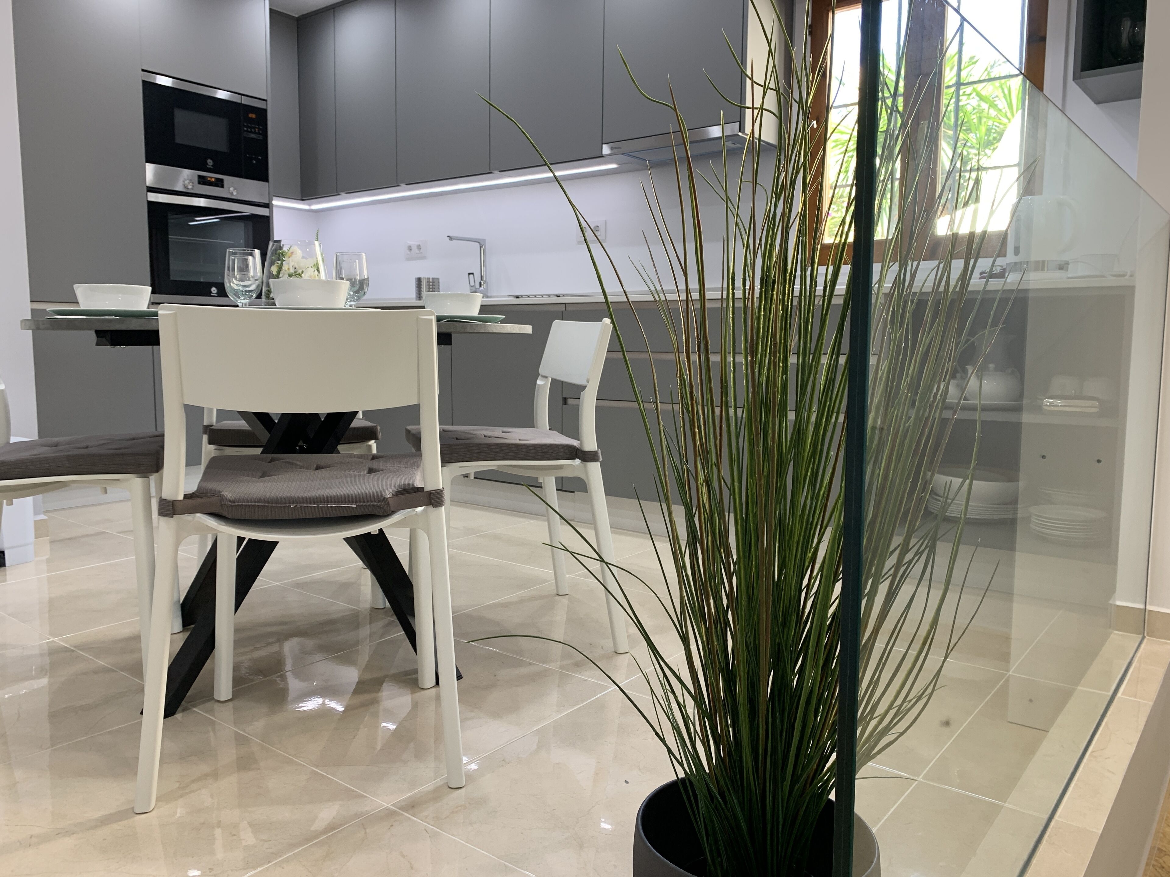 A modern kitchen with white chairs, a dining table, and a potted plant.