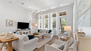 A spacious living room with white furniture, a television, and large windows. - Camp District | Access to WaterColor Amenities (Santa Rosa Beach)