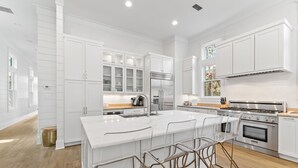 A modern kitchen with white cabinetry, a large island with bar stools, stainless steel appliances, and a wooden floor. - Camp District | Access to WaterColor Amenities (Santa Rosa Beach)
