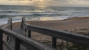 A wooden boardwalk leading to a beach with the ocean and a cloudy sky in the background. - 	Modern luxury meets coastal comfort-1200 sq.ft  completely remodeled. Pool (Ormond Beach)