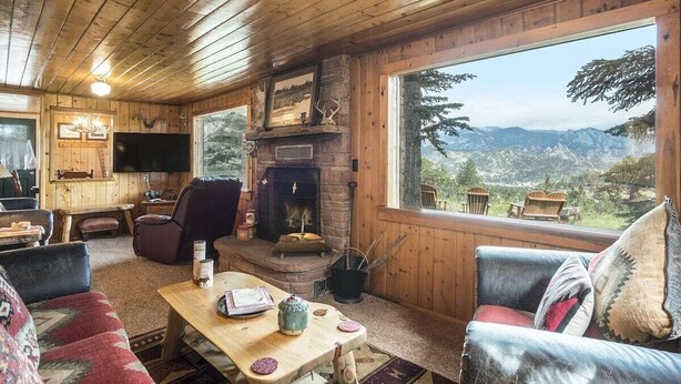 L’intérieur chaleureux d’un chalet avec une cheminée, des murs en bois et une grande fenêtre donnant sur une vue imprenable sur les montagnes.