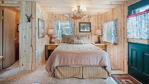 Une chambre à coucher aux murs lambrissés, avec un lit, deux tables de chevet, un lustre et une porte ornée d’une tête de cerf.