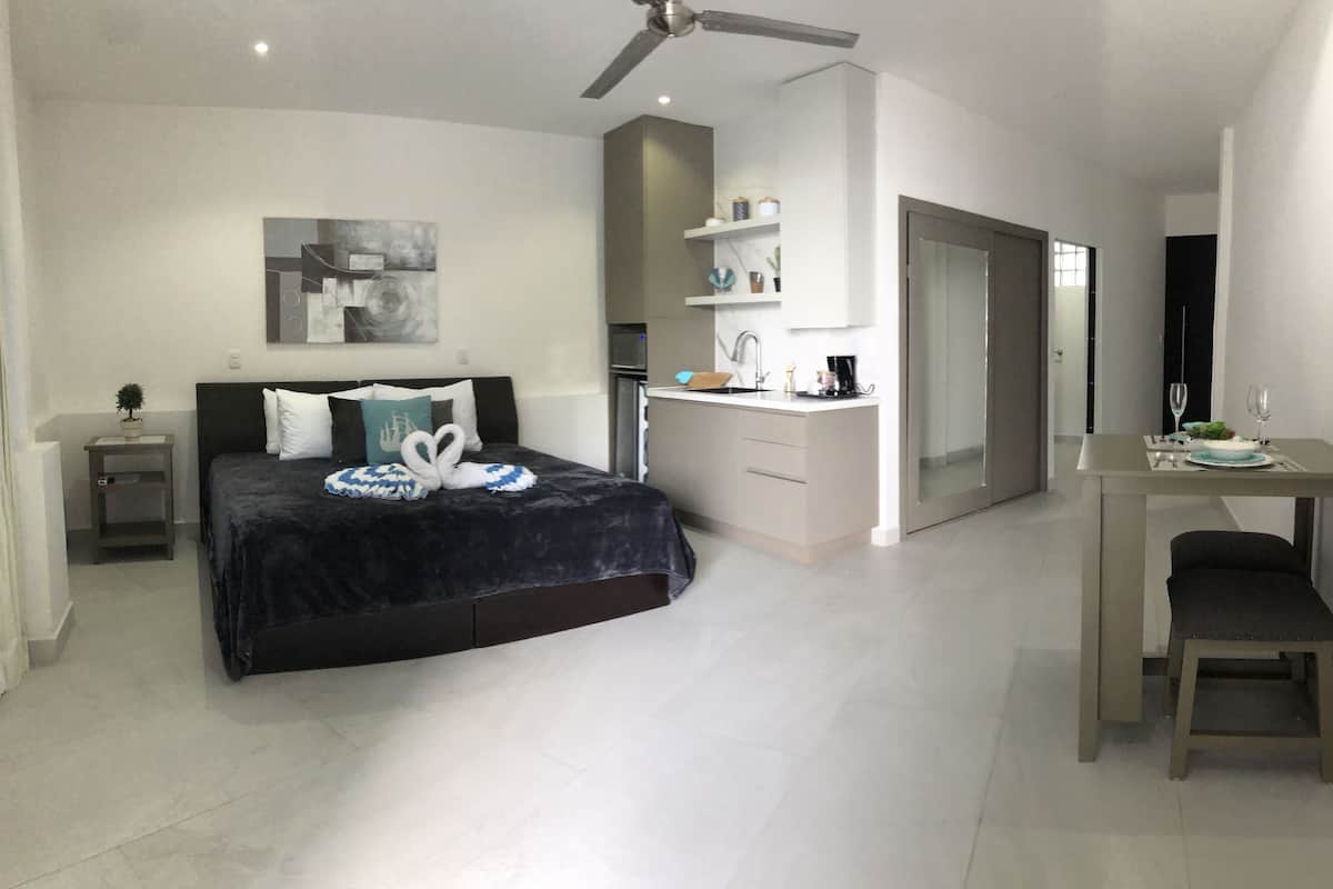 A modern hotel room with a bed, a desk, and a kitchenette.