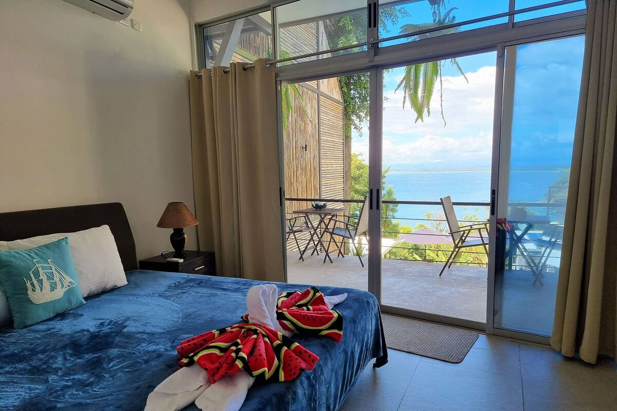 A bedroom with a bed, a nightstand, a lamp, and a view of an outdoor patio with a table and chairs.