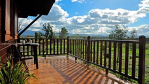 Una terraza de madera con vista a un campo verde y montañas a lo lejos.