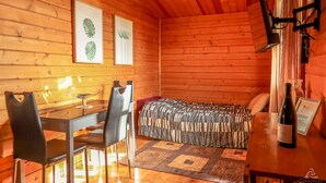 Una habitación acogedora de madera con una cama, un escritorio con sillas y una botella de vino sobre una mesita.