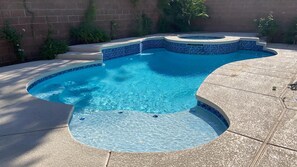 A swimming pool with a curved design, surrounded by a stone deck and a brick wall.