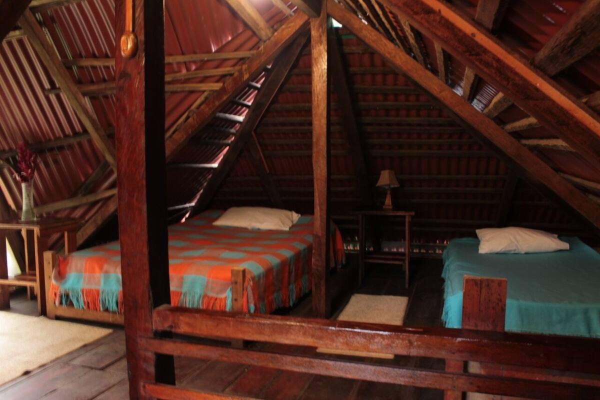 A rustic attic bedroom with two beds, wooden beams, and a sloped ceiling.