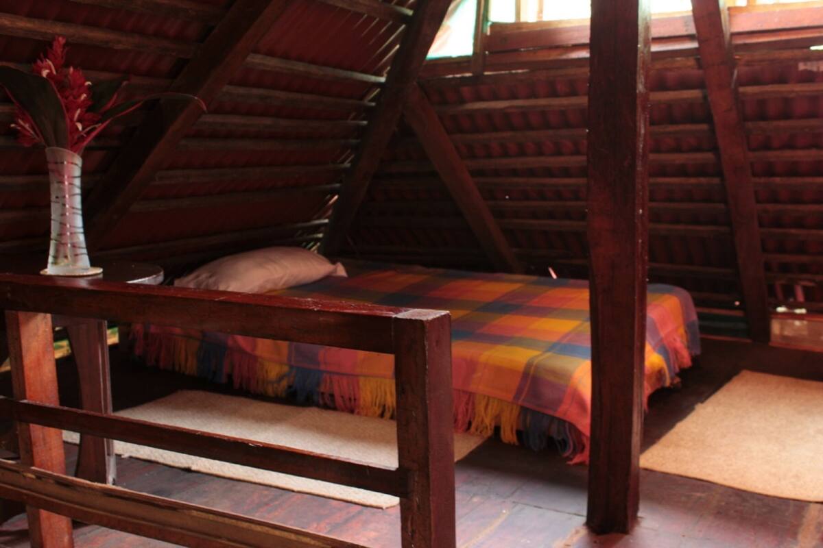 A cozy attic bedroom with a wooden bed, a colorful blanket, and a vase with flowers.