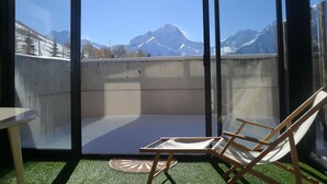 Un balcón con vistas a montañas nevadas, una silla de madera y una mesita.