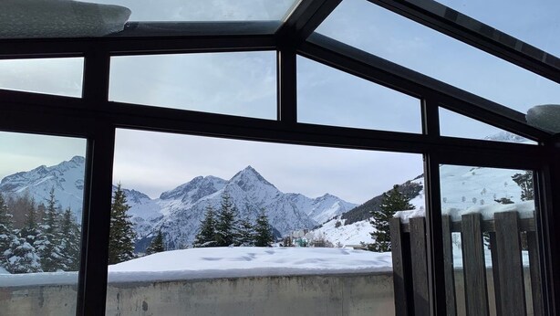 Vista a través de una ventana que muestra un paisaje nevado, con montañas y árboles.