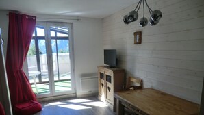 Una habitación con una mesa de madera, un televisor sobre un mueble bajo y un ventanal corredero hacia el exterior.