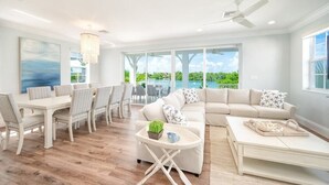A spacious living room with a large window, a dining area, and a ceiling fan.