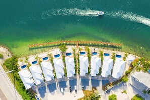 Vista aérea de un resort con múltiples bungalows sobre el agua, dispuestos en forma de semicírculo, conectados por una pasarela de madera, con un bote visible en el agua.