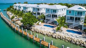 A row of waterfront houses with a dock extending into the water, a swimming pool, and a clear view of the ocean.