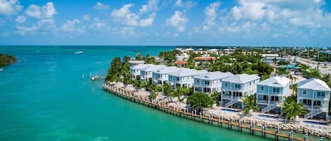 A coastal resort with multiple light blue buildings connected by a dock, surrounded by turquoise waters and palm trees.