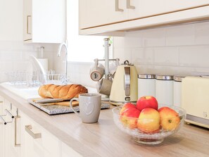Una cocina con pan, una taza, un hervidor, un tostador y un bol de fruta.
