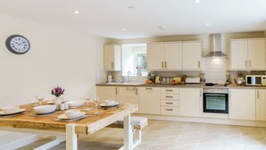 A modern kitchen with white cabinets, a wooden dining table, and a built-in oven.