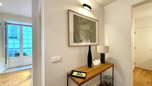 En hall med ett konsolbord i trä, ett inramat citat på väggen, en lampa och en liten papperskorg.