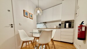Ett modernt kök med vita skåp, ett runt bord i glas och två vita stolar. En brandsläckare är monterad på väggen.