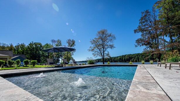 Una piscina con agua cristalina, rodeada por una terraza de piedra y sillones de descanso.