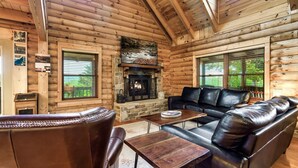 A log cabin interior with a stone fireplace, leather furniture, and wooden walls. - Drive in Theater! Putt-Putt | Fire Pit | Top 10% (Sevierville)