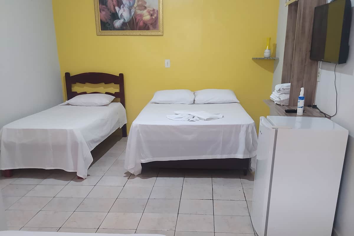A hotel room with two single beds, a double bed, a small refrigerator, and a wooden wardrobe.