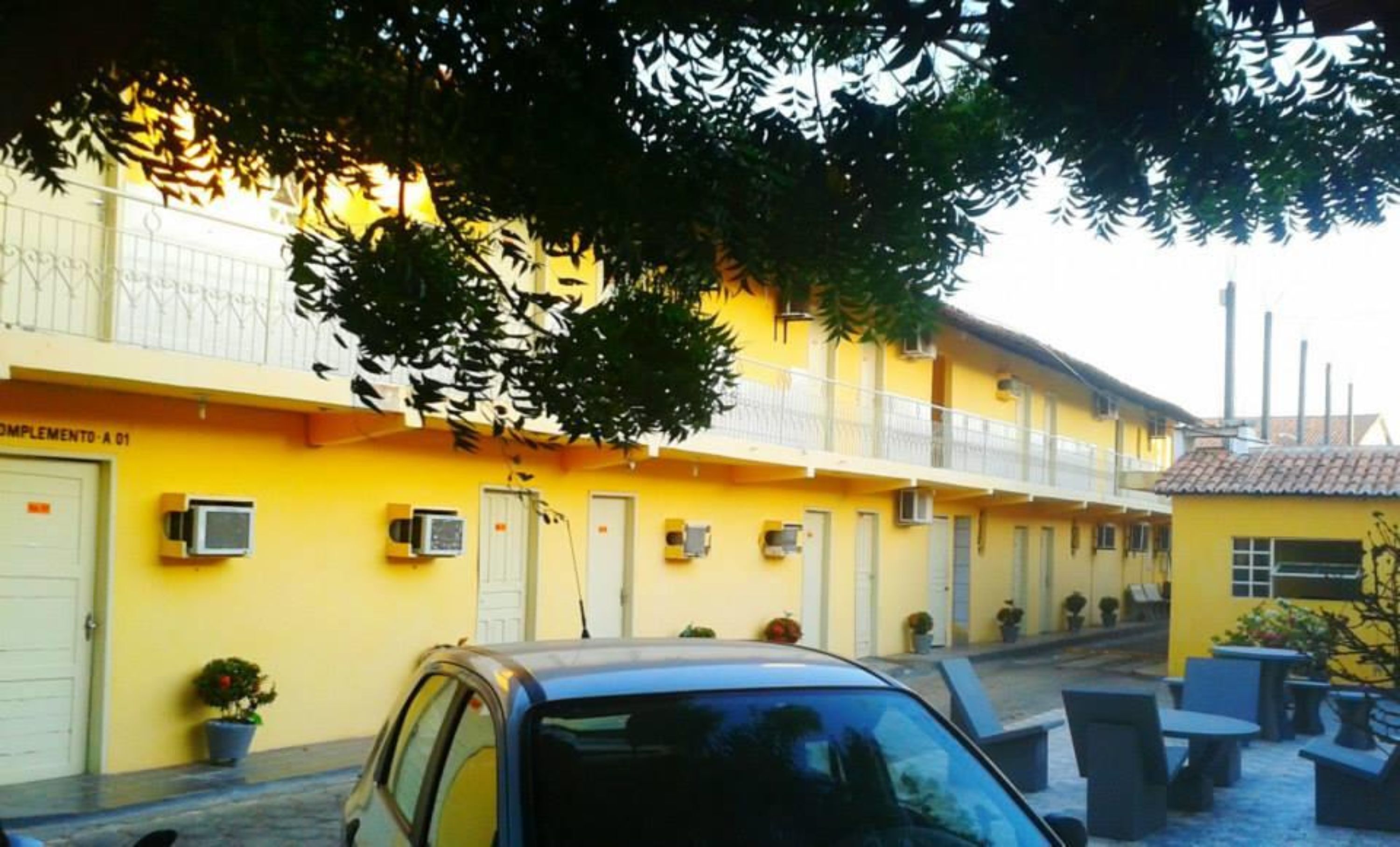 A yellow building with a balcony, air conditioning units, and potted plants.