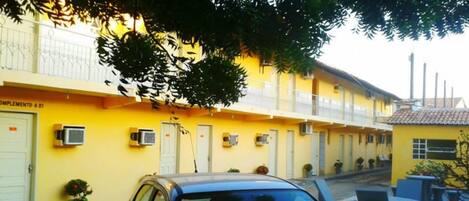 A yellow building with a balcony, air conditioning units, and potted plants.
