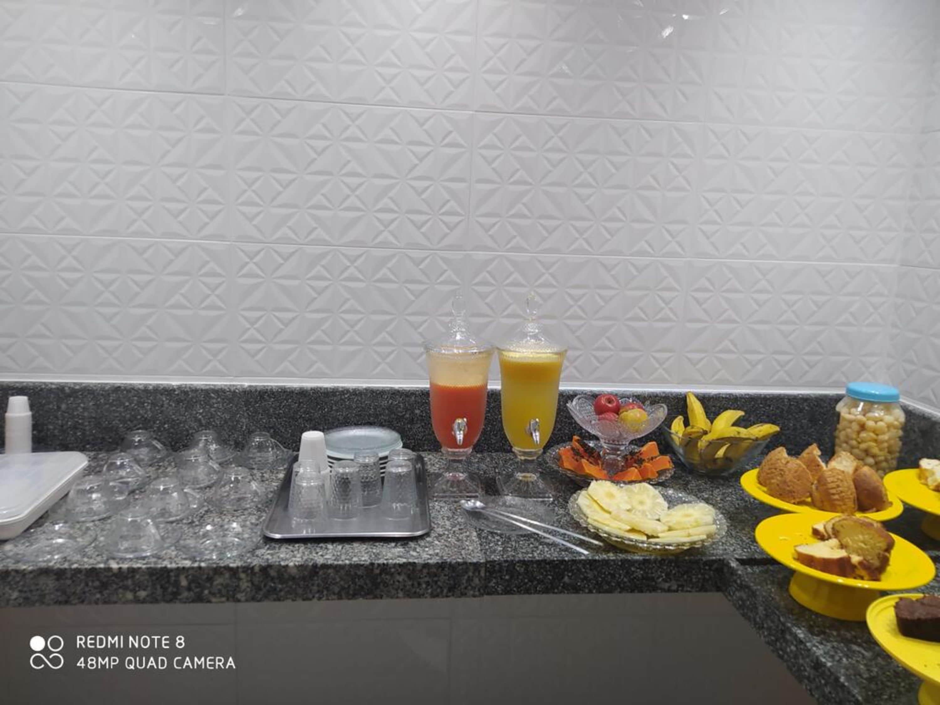 Una encimera de cocina con diversos alimentos y bebidas, incluyendo un vaso de zumo de naranja y un vaso de bebida roja.
