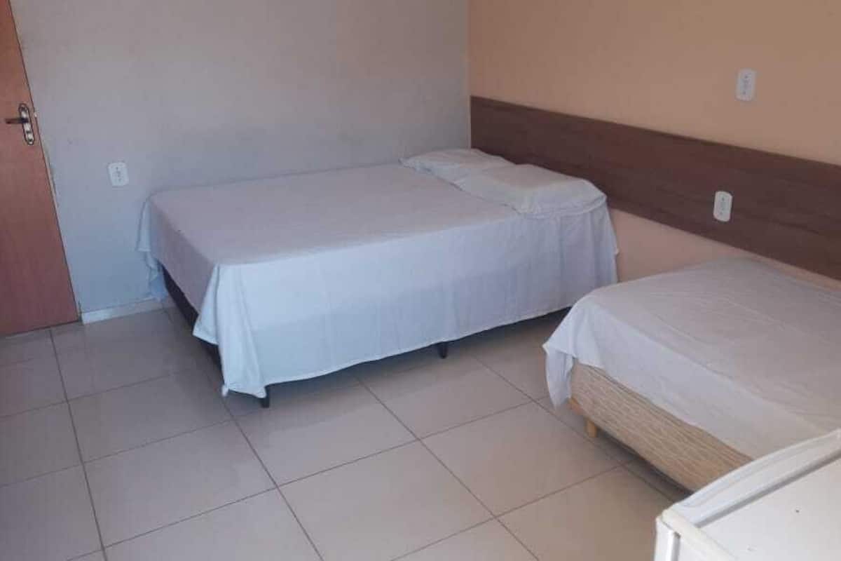 A room with two single beds, a wooden headboard, and a tiled floor.
