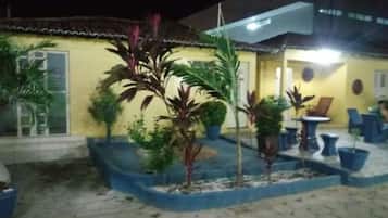 A yellow building with a tiled roof, outdoor seating area, and potted plants.