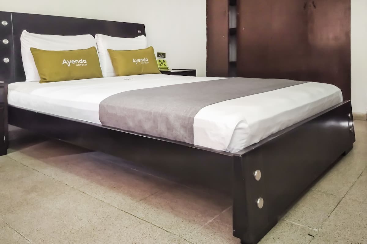 Een bed met donker frame, witte beddengoed en twee groene kussens met de tekst 'Ayenda Hotels'.