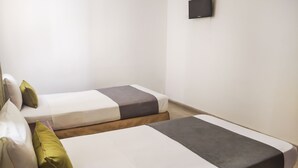 Two single beds with white and gray bedding, a small wall-mounted TV, and a plain white wall. - Ayenda 1622 Charmin (Santa Marta)