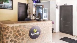 A reception desk with a stone facade, a digital screen, and a sign for Ayenda Hotels. - Ayenda 1622 Charmin (Santa Marta)