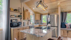 A modern kitchen with wooden cabinets, a granite countertop, stainless steel appliances, and a seating area with a view.